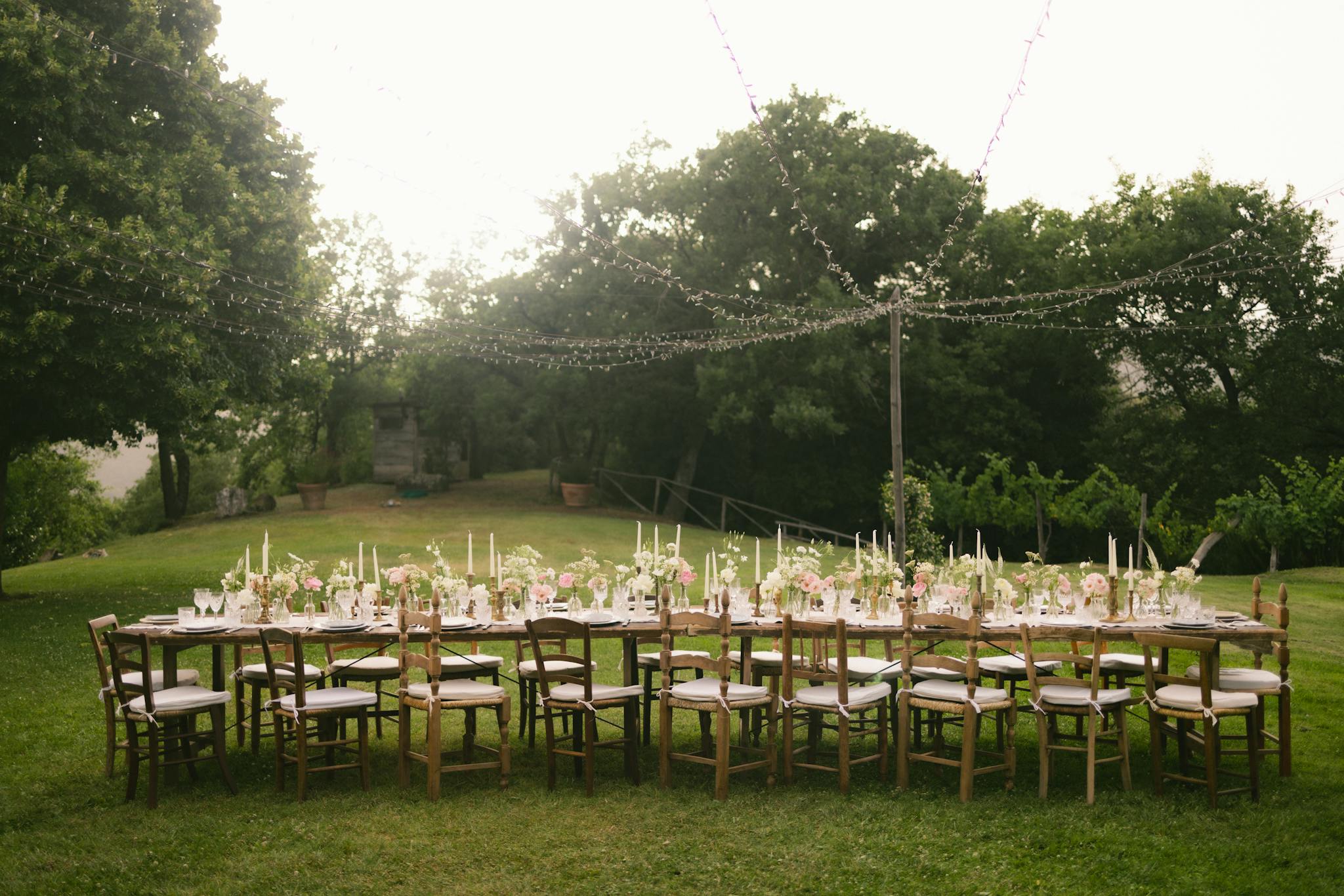 Beautiful outdoor wedding reception table setup with floral decorations and string lights in a garden.